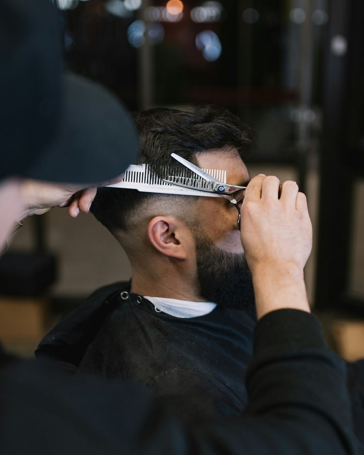 Barbeiro aparando a barba de um cliente com tesoura e pente
