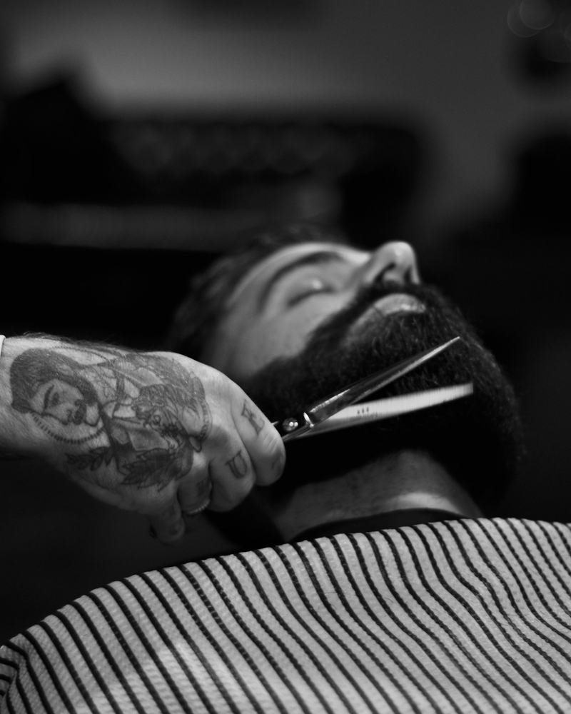 Barbeiro aparando a barba de um cliente com tesoura