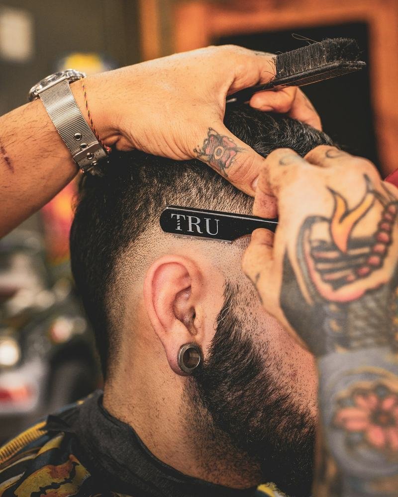 Barbeiro tatuado desenhando o contorno da barba com navalha