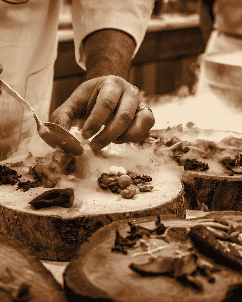 Cozinheiro finalizando um prato sobre madeira, com vapor subindo